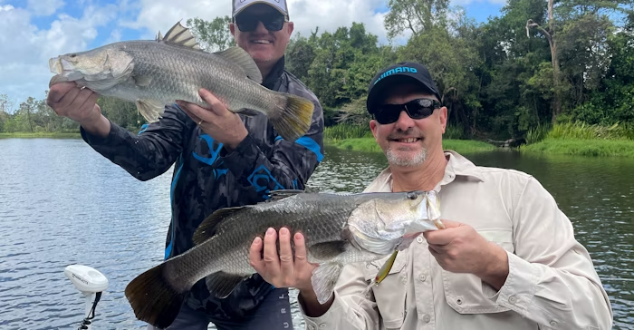 Two anglers proudly holding trophy Barramundi catches, sharing expert tips and tactics for mastering impoundment Barramundi fishing